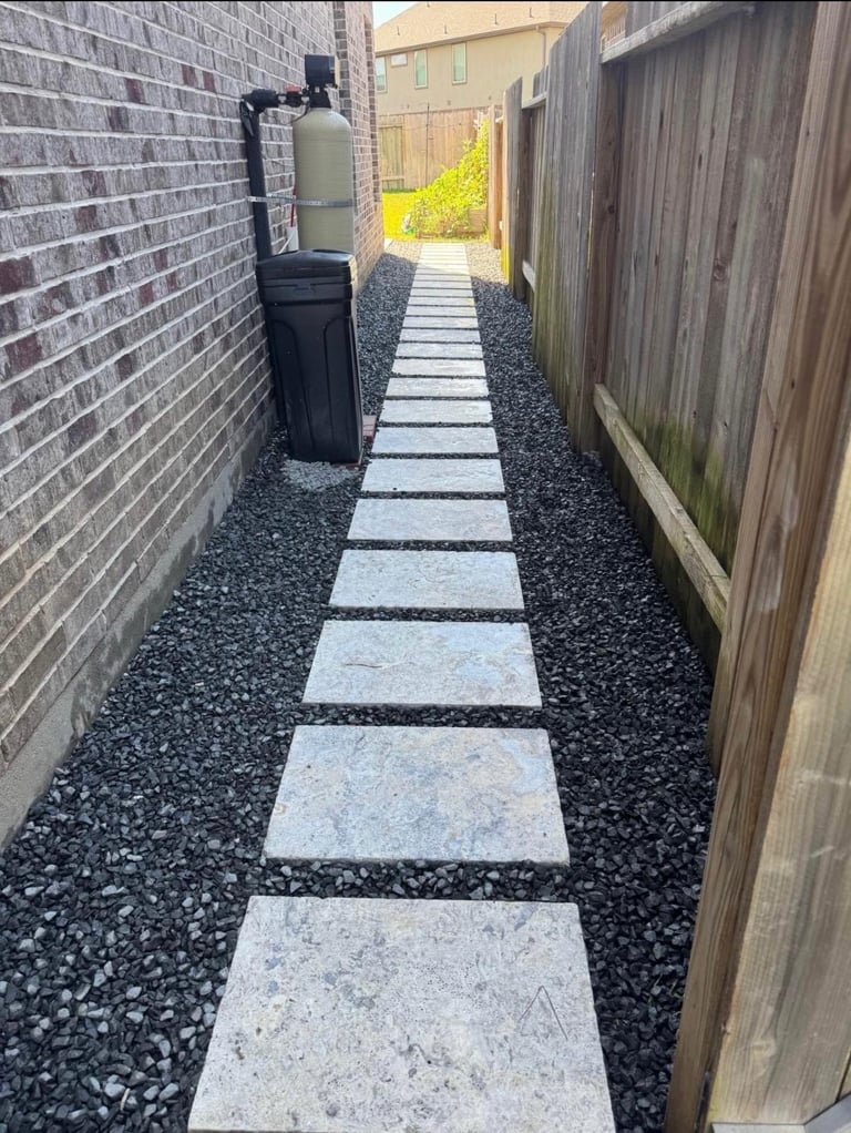 Narrow side yard pathway with stepping stones and dark gravel between brick wall and wooden fence